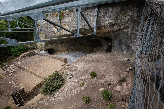 A birds-eye view of a cave behind what looks like the foundations of a building