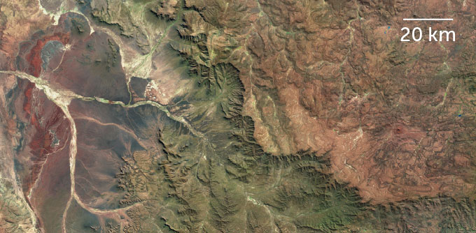 An aerial view of a landscape, with a brown plateau on the right and greener foothills on the left.